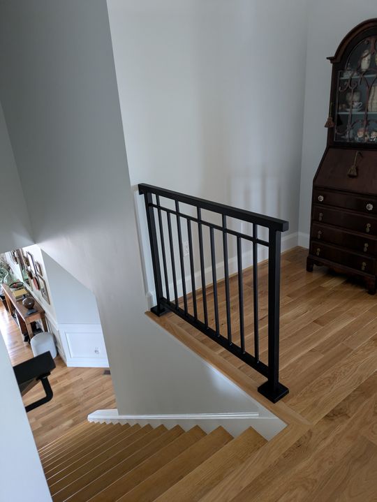 Interior staircase with black metal railing, wooden floors, and antique cabinet on upper landing
