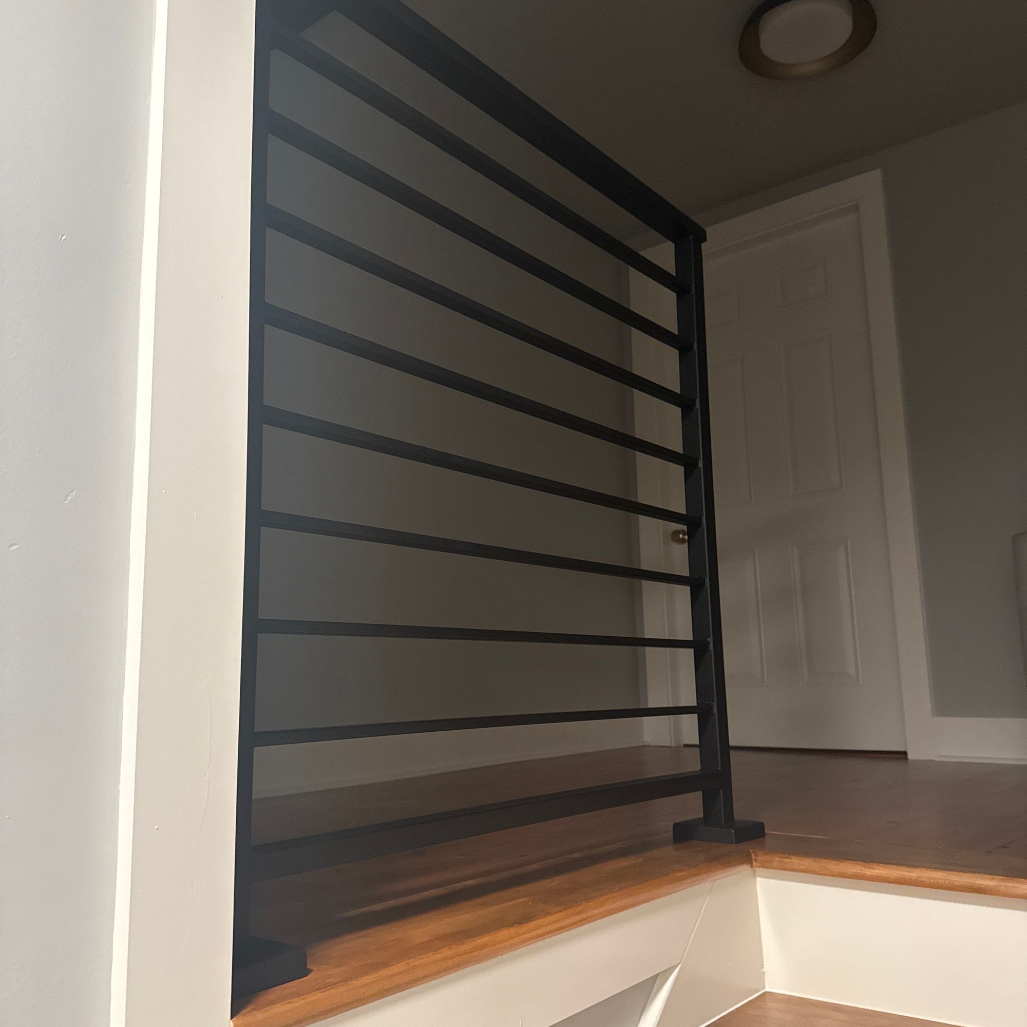 Modern staircase with white steps, wooden handrail, and black metal railing leading upward in a bright interior space