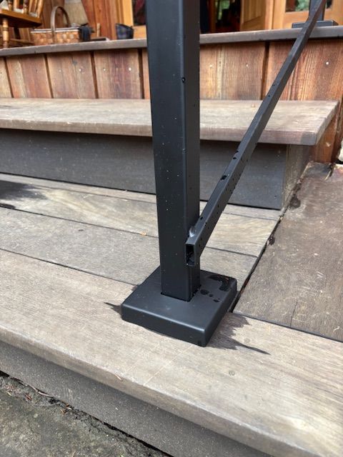Black metal railing post with mounting bracket installed on wooden deck steps