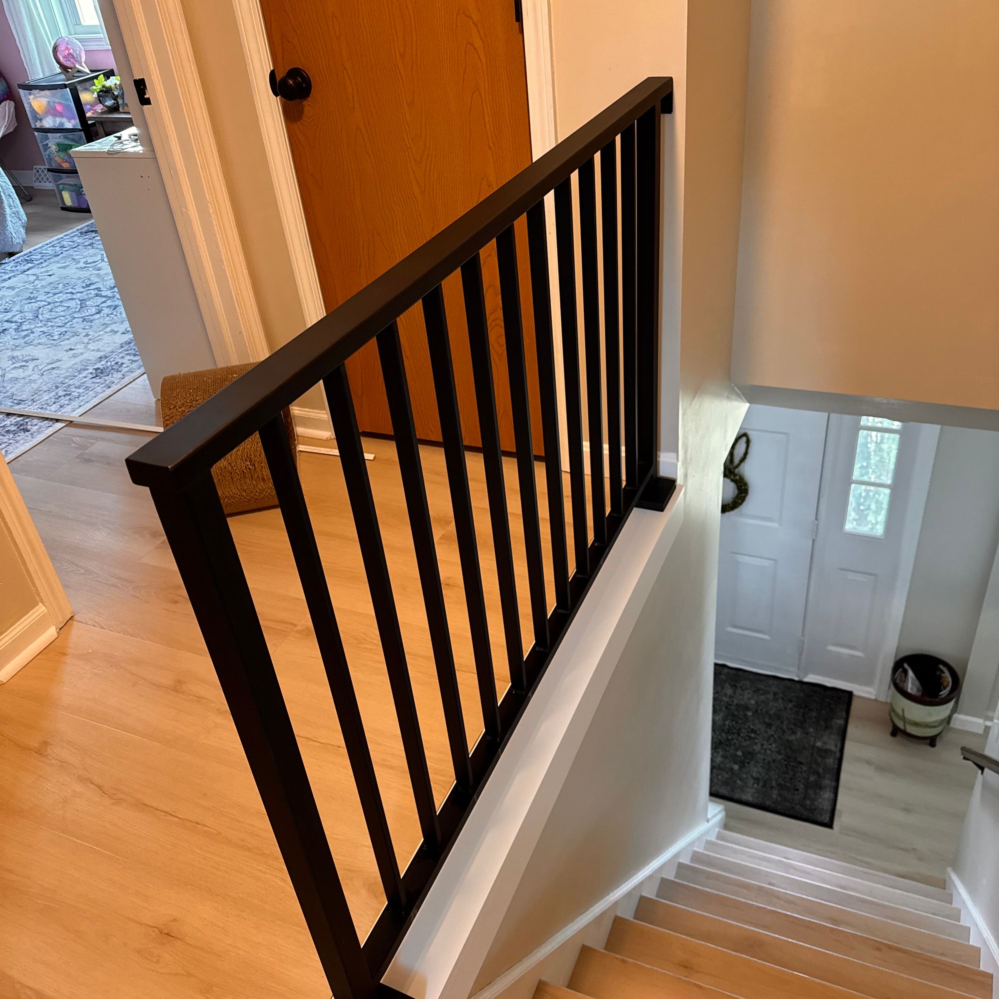 Interior staircase with black metal railing and vertical spindles, wooden steps, and white walls leading to upper floor of home