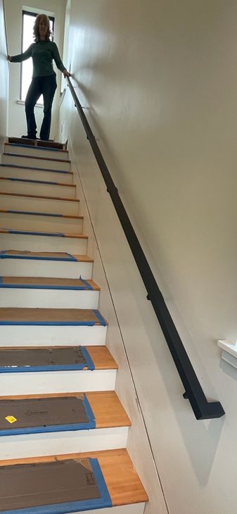 Person standing on wooden stairs with blue painter's tape, holding onto a black handrail during home renovation
