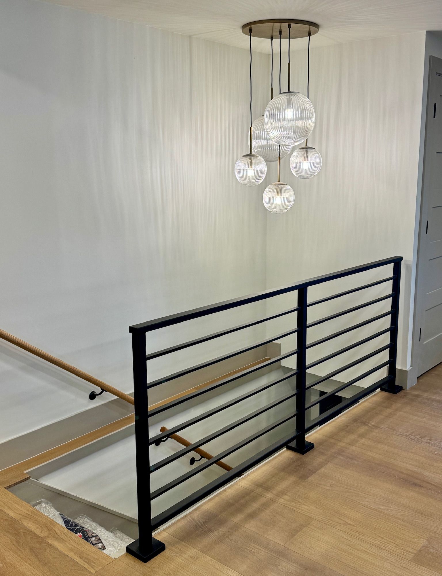 Modern staircase landing with black metal railing, wood handrail, and contemporary pendant light fixture with multiple glass globes