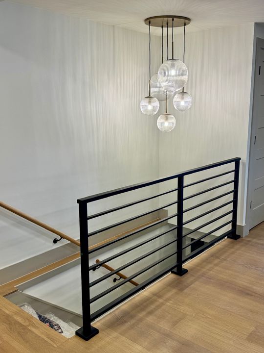 Modern staircase landing with black metal railing, wood handrail, and contemporary pendant light fixture with multiple glass globes
