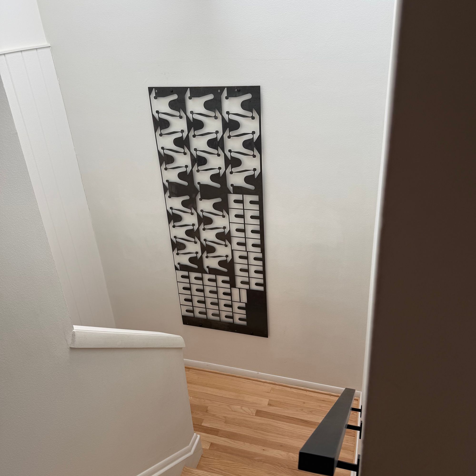 Staircase with wooden steps, white walls, and black and white geometric artwork on the wall
