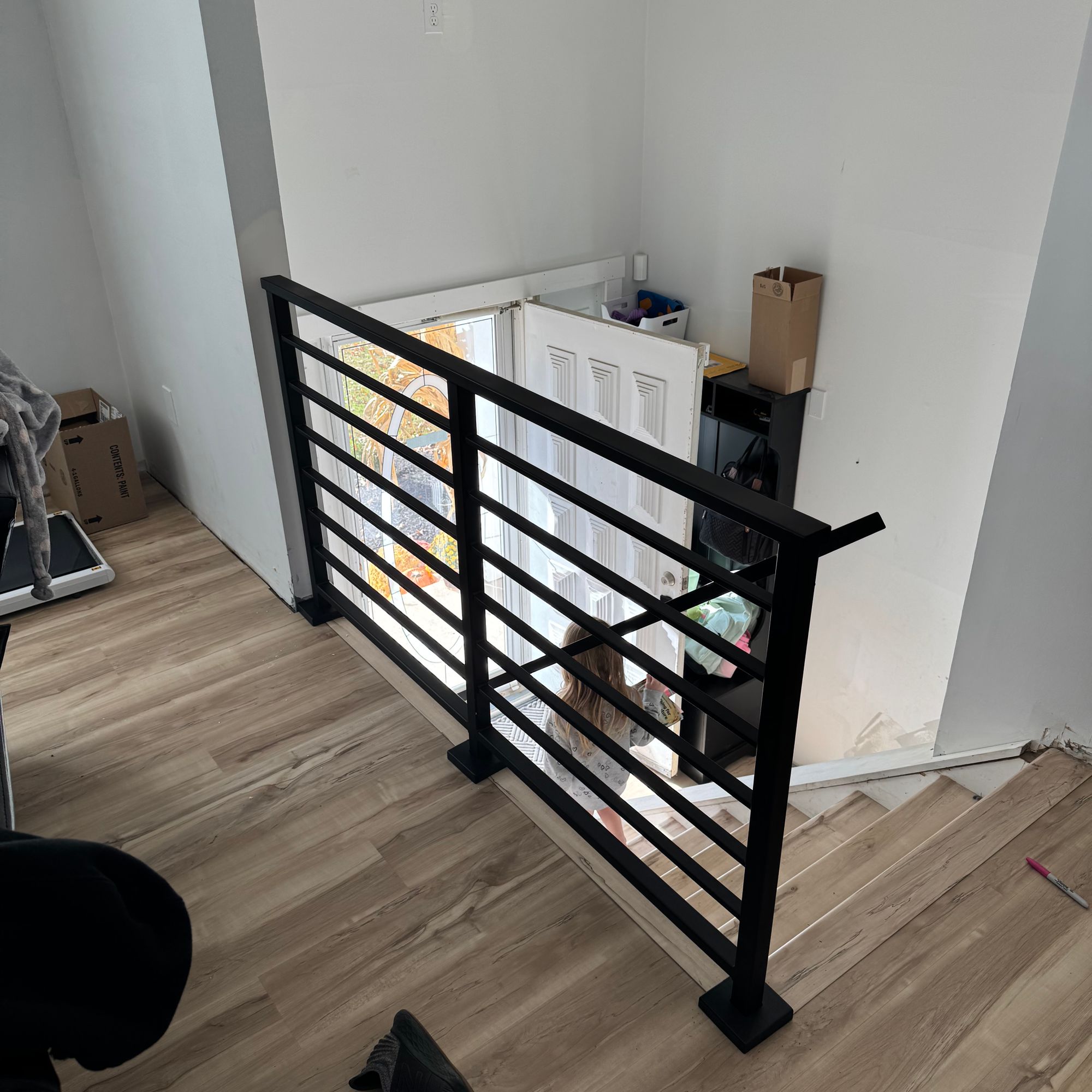 Modern black metal stair railing with horizontal slats on wooden floor in white-walled interior space
