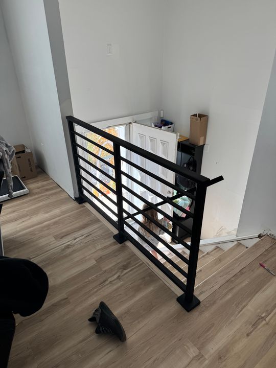 Modern black metal stair railing with horizontal slats on wooden floor in white-walled interior space