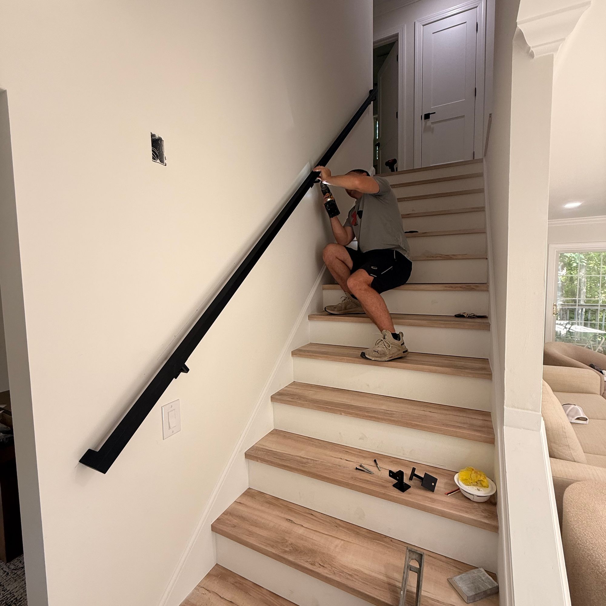 Person installing handrail on wooden staircase in modern home interior