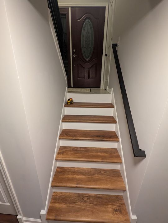 Staircase with wooden treads and white risers leading up to a front door with decorative glass panel