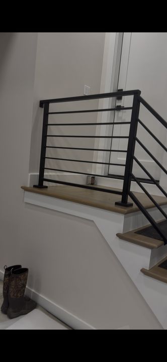 Modern staircase with black metal horizontal railings, white walls, and wooden stair treads in an interior home setting