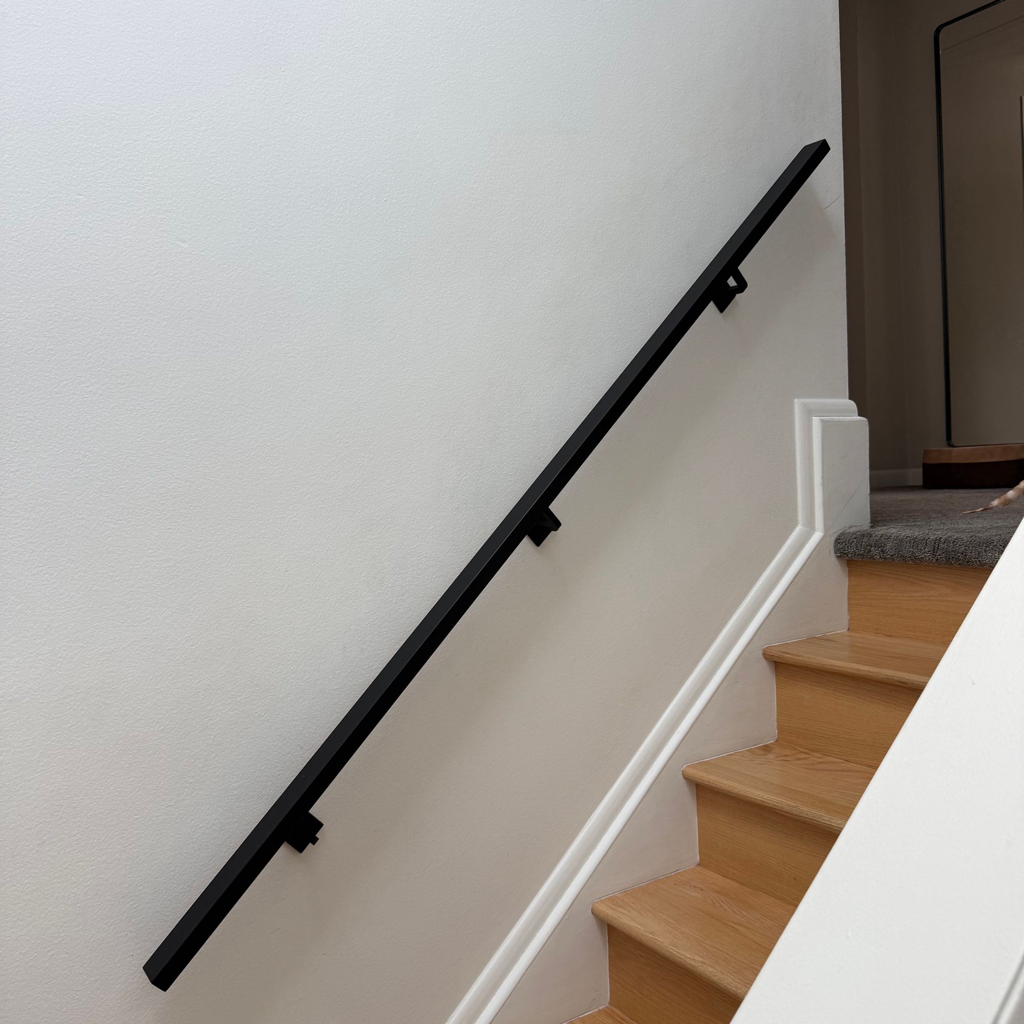 Modern staircase with wooden steps, white walls, and black handrail mounted on wall