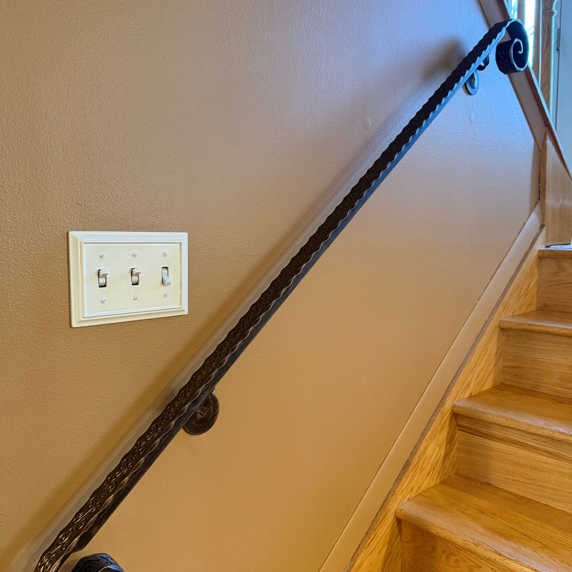 Wooden staircase with decorative black metal handrail and light switch on beige wall