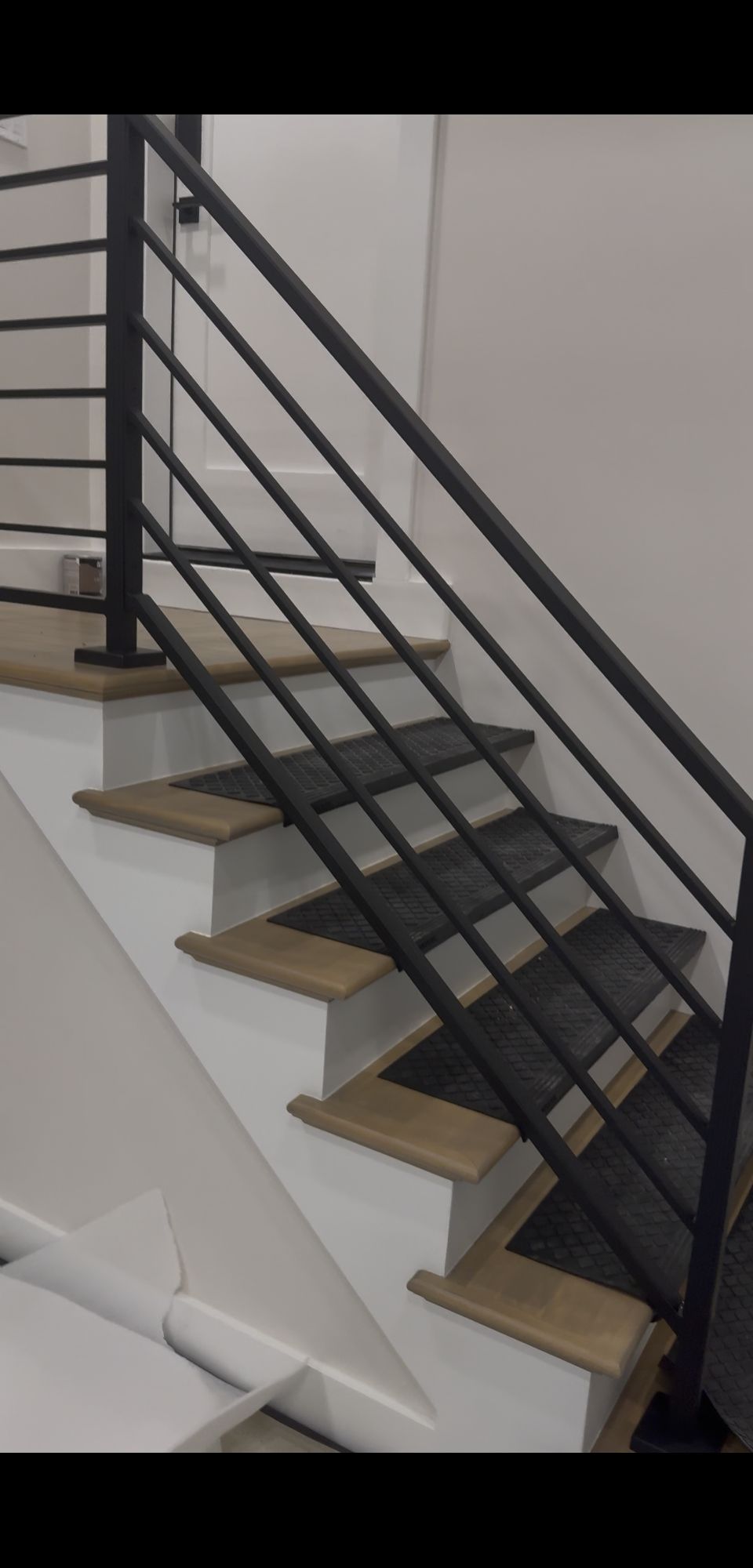 Modern staircase with wooden treads, white risers, and black metal horizontal railing in an interior space