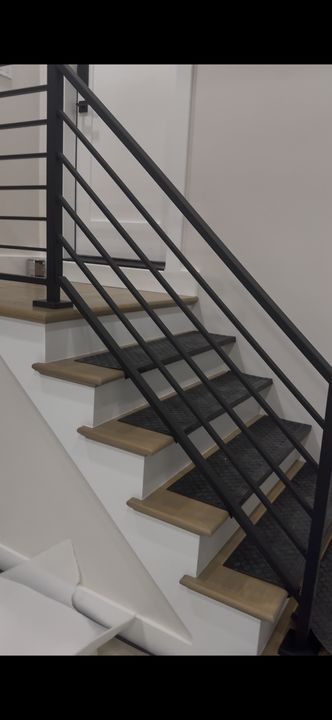 Modern staircase with wooden treads, white risers, and black metal horizontal railing in an interior space