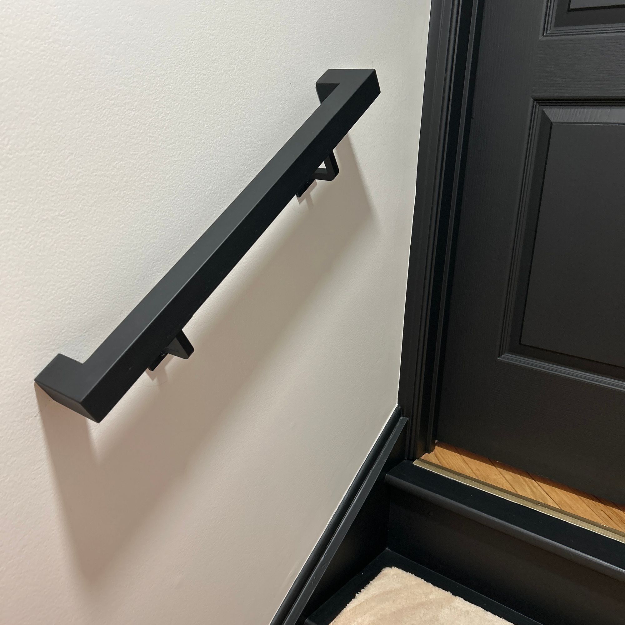 Black handrail mounted on white wall next to dark door and staircase