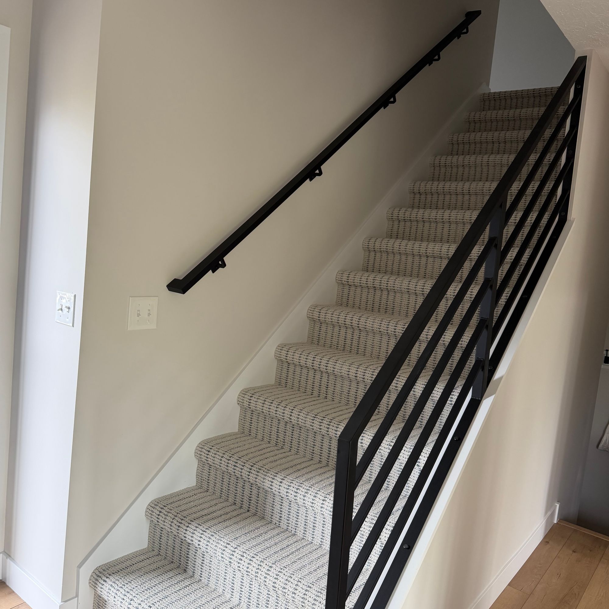 Interior staircase with beige patterned carpet runner and black metal railing leading upstairs in a modern home