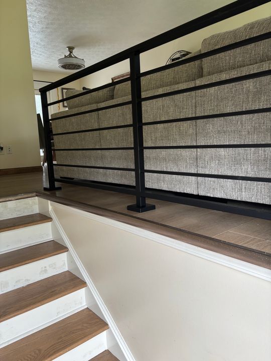 Modern staircase with black metal railing, wood steps, and fabric panel inserts leading to upper floor