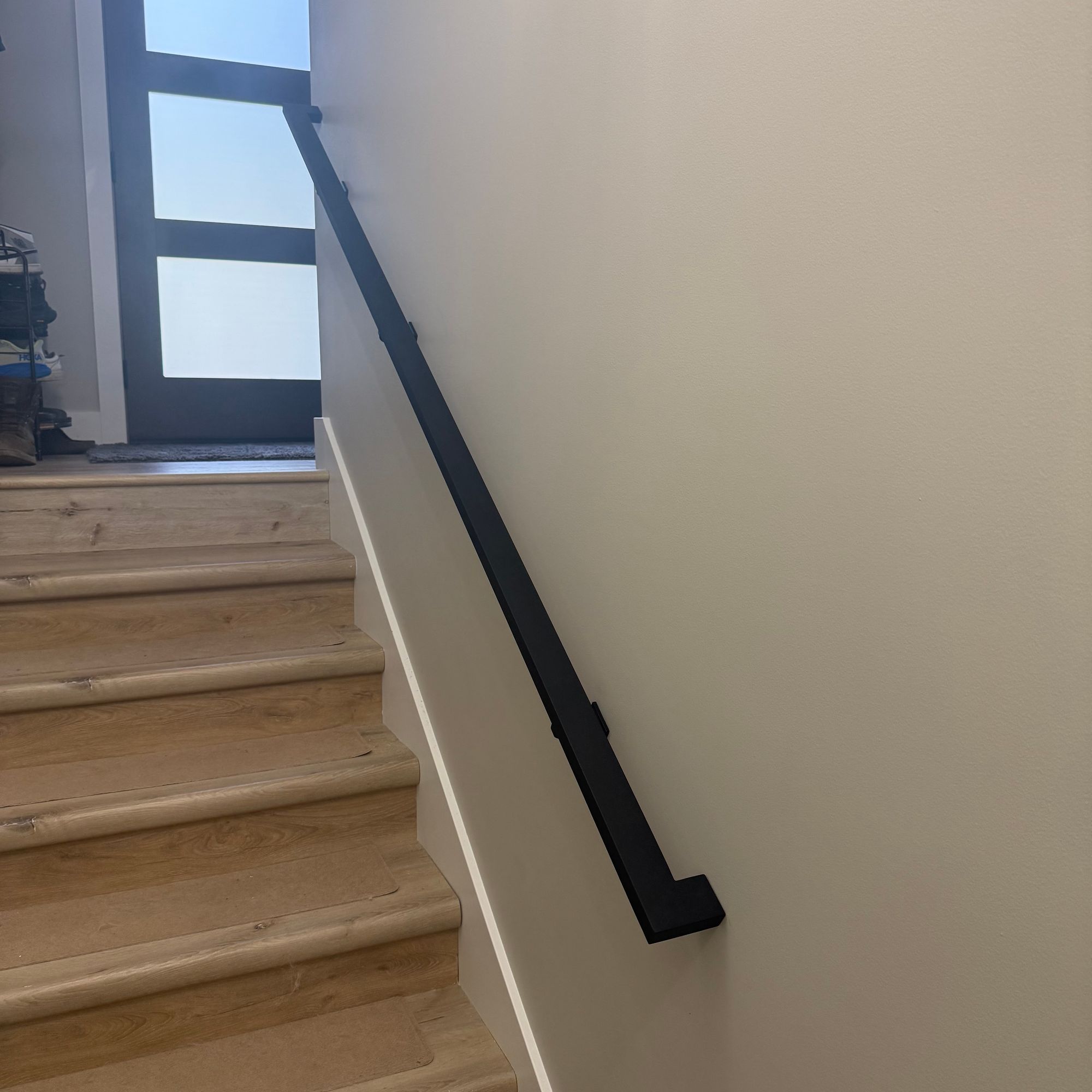 Interior staircase with wooden steps, black metal handrail mounted on white wall, and modern glass-panel door visible at the top