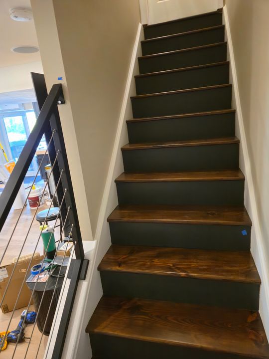 Interior staircase with dark green painted risers and natural wood treads, featuring black metal railings and white walls in a modern home under construction