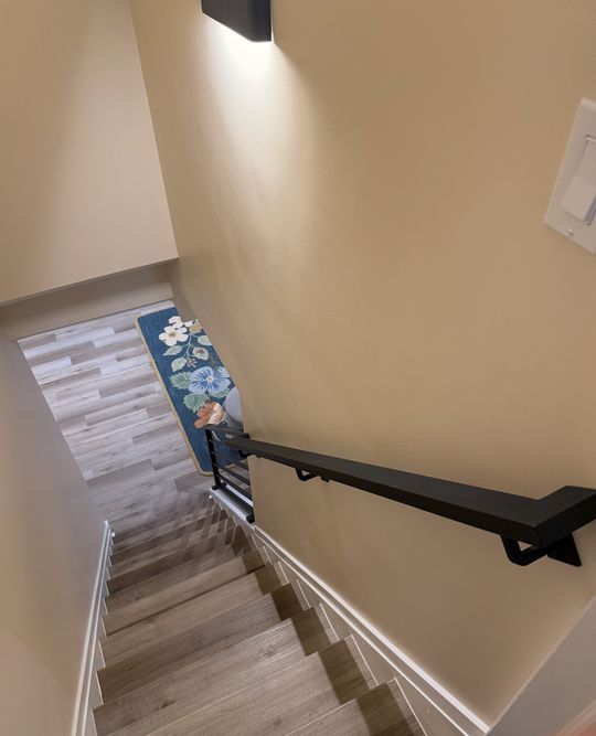 Interior staircase with beige walls, dark handrail, and decorative floral artwork on the wall