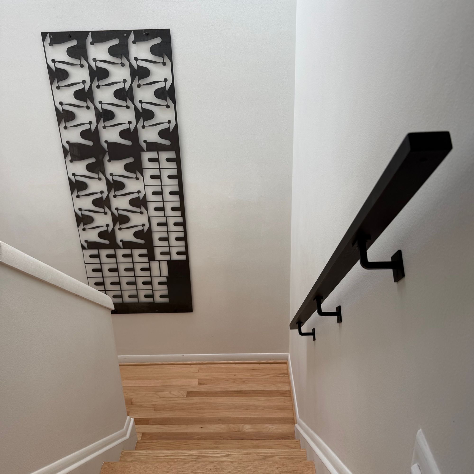 A modern staircase with wooden steps, white walls, and black handrail, featuring decorative black and white patterned artwork on the wall