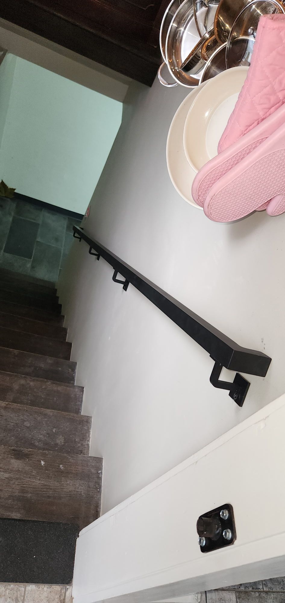 Interior staircase with dark wooden steps, black metal handrail, white walls, and pink decorative items visible on upper level