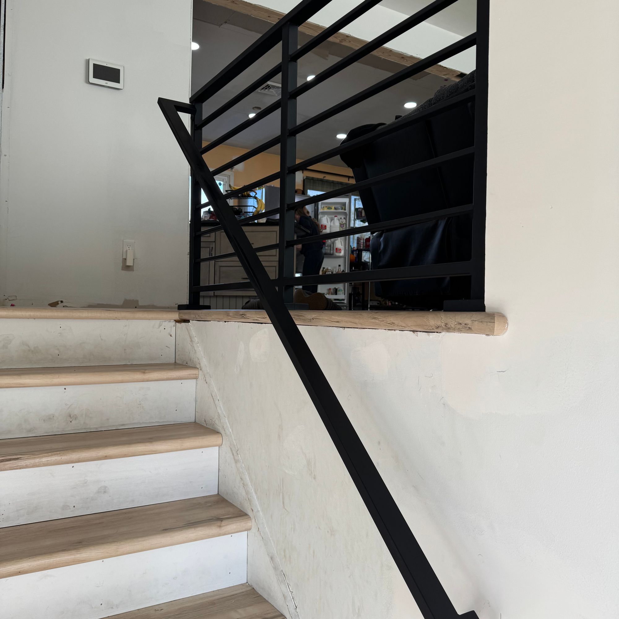 Modern staircase with white concrete steps, wooden treads, and black metal railing leading to upper level
