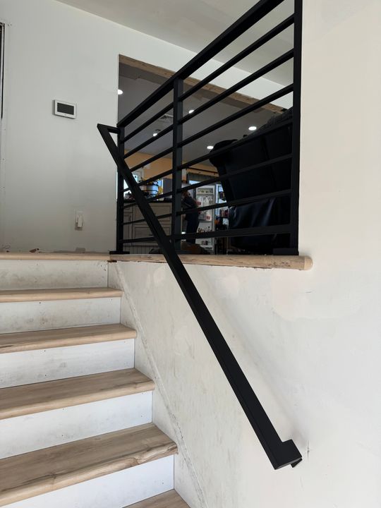 Modern staircase with white concrete steps, wooden treads, and black metal railing leading to upper level