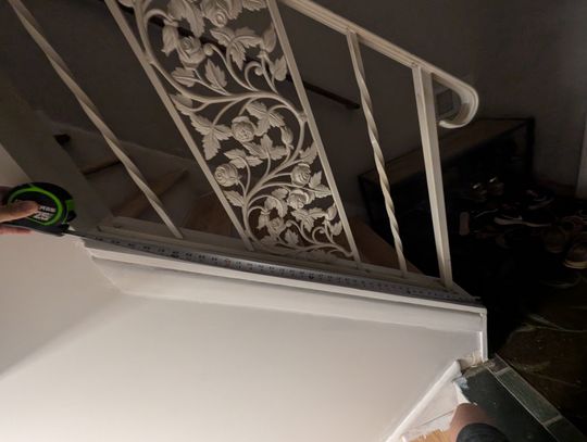 Ornate white metal stair railing with decorative floral scrollwork pattern being installed or repaired in an indoor setting