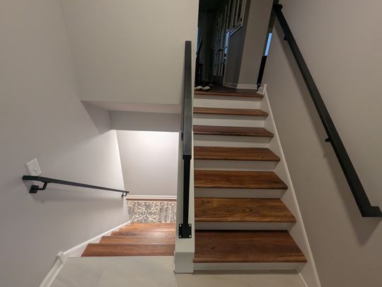 Modern staircase with wooden treads, white risers, and black metal handrail leading to upper floor