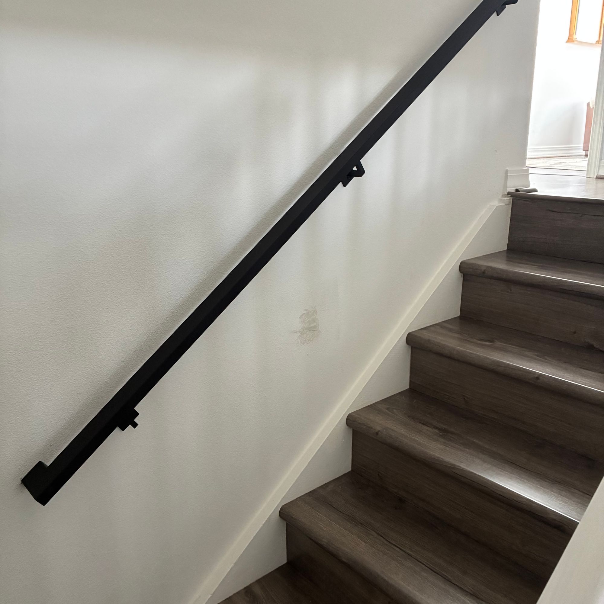 A staircase with dark wood steps and a black metal handrail mounted on a white wall, with natural light coming from a window at the top