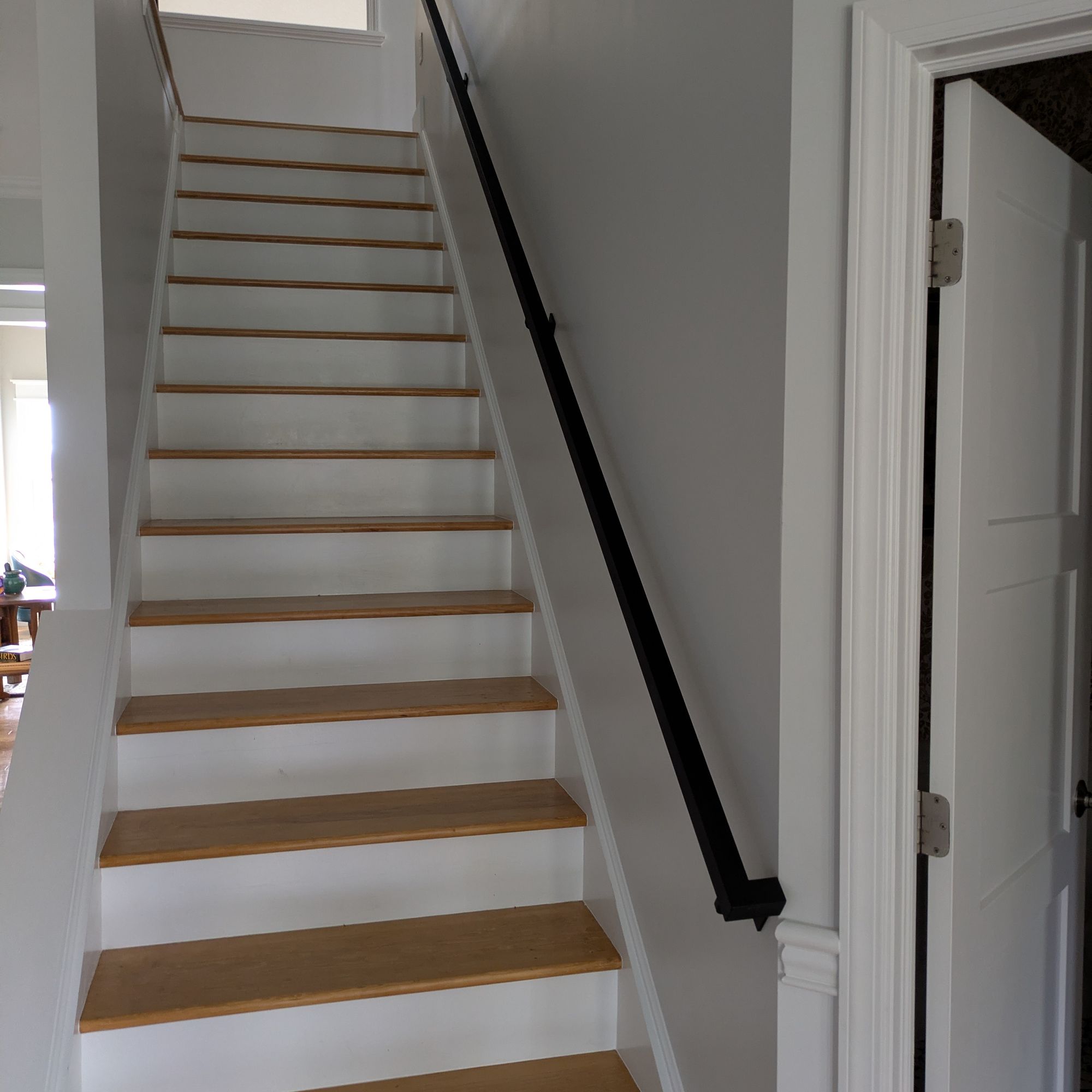 Interior staircase with white risers, natural wood treads, black handrail, and gray walls leading to upper floor