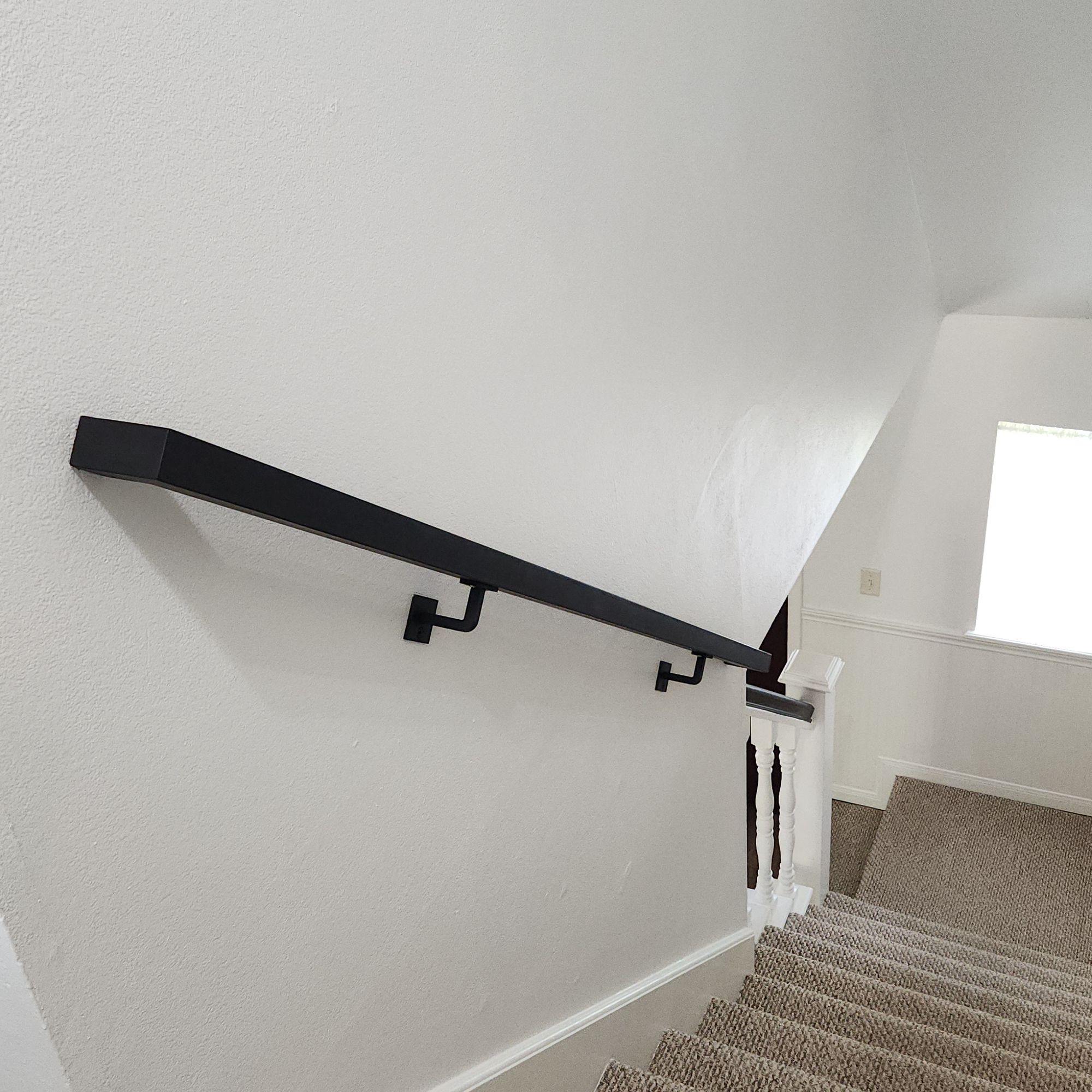 Interior staircase with black handrail, white walls, and brown carpet runner going down the steps