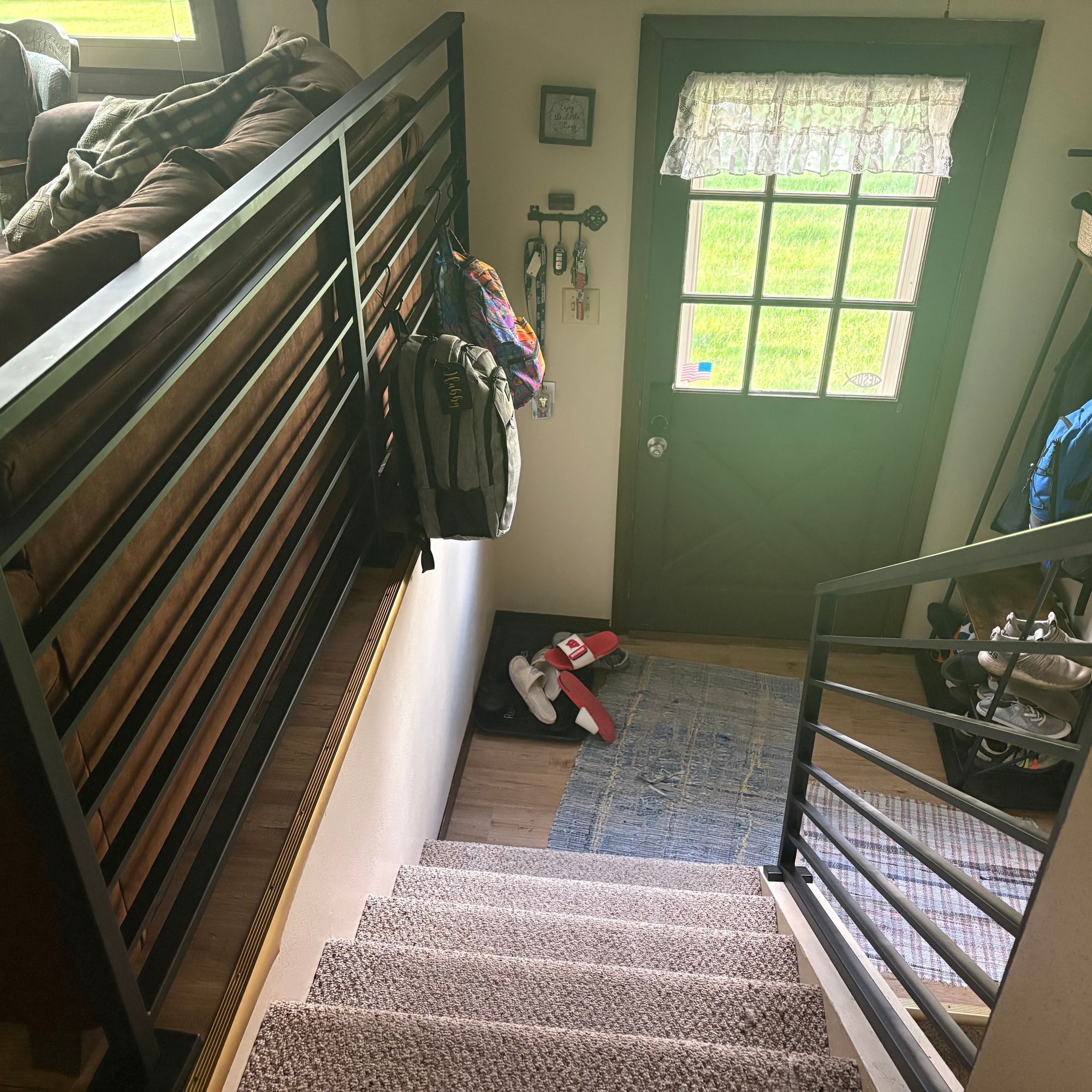A bedroom with bunk beds featuring metal railings, a green door with window, and carpeted stairs leading down from an upper level