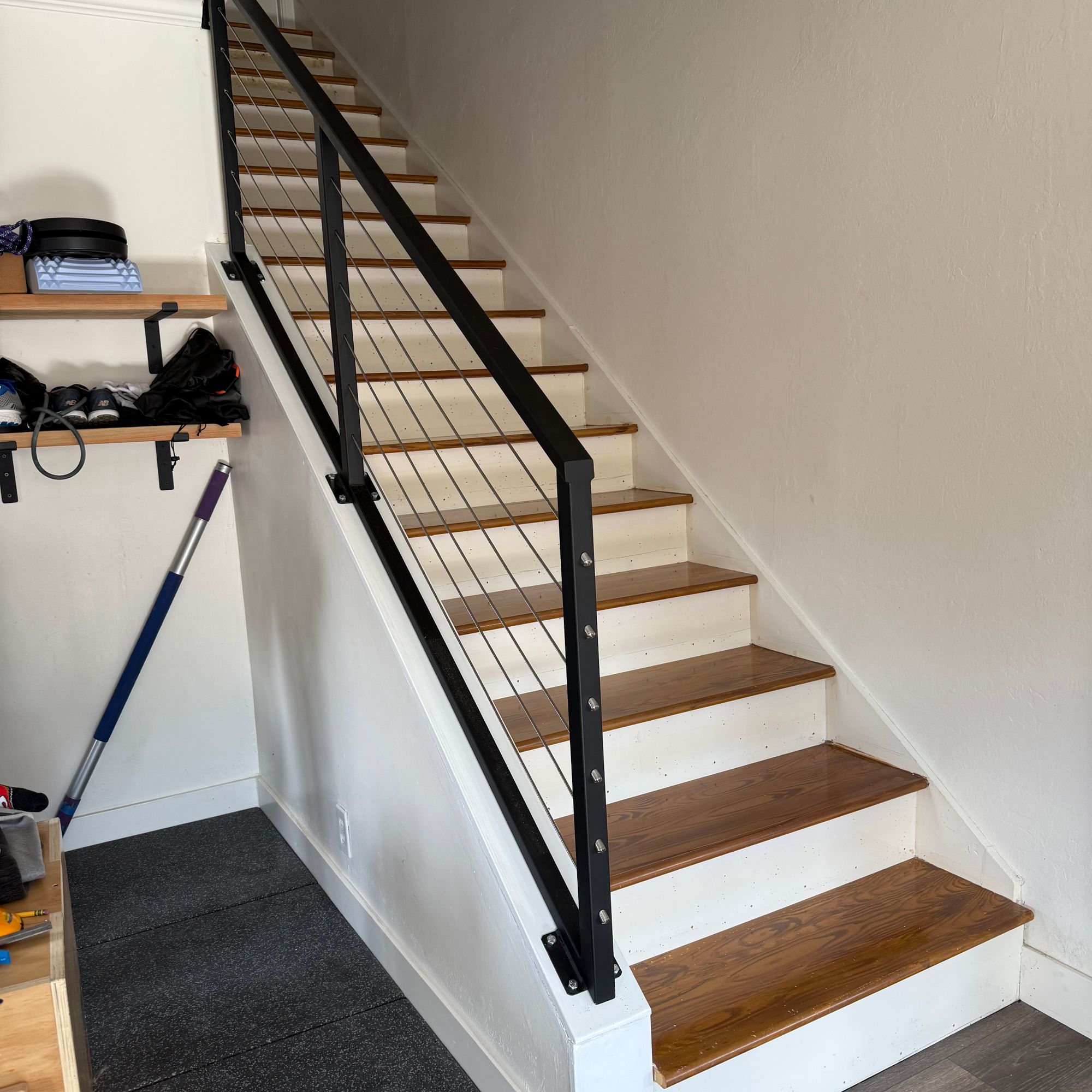 Modern staircase with wooden treads, white risers, and black metal railing with horizontal cable wires in a home interior