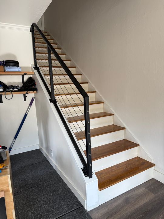 Modern staircase with wooden treads, white risers, and black metal railing with horizontal cable wires in a home interior