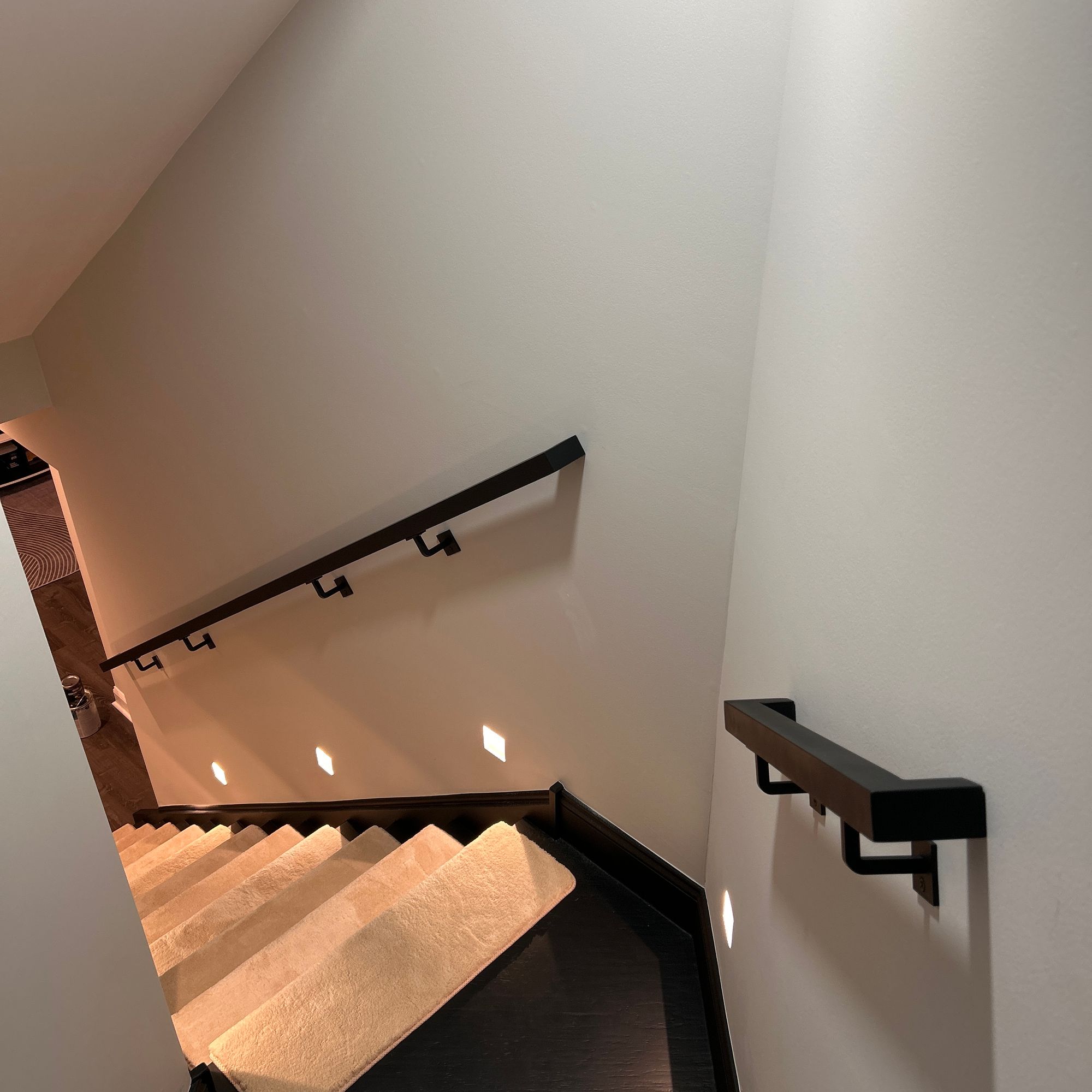 Modern staircase with black handrails, white walls, and warm lighting descending to lower level