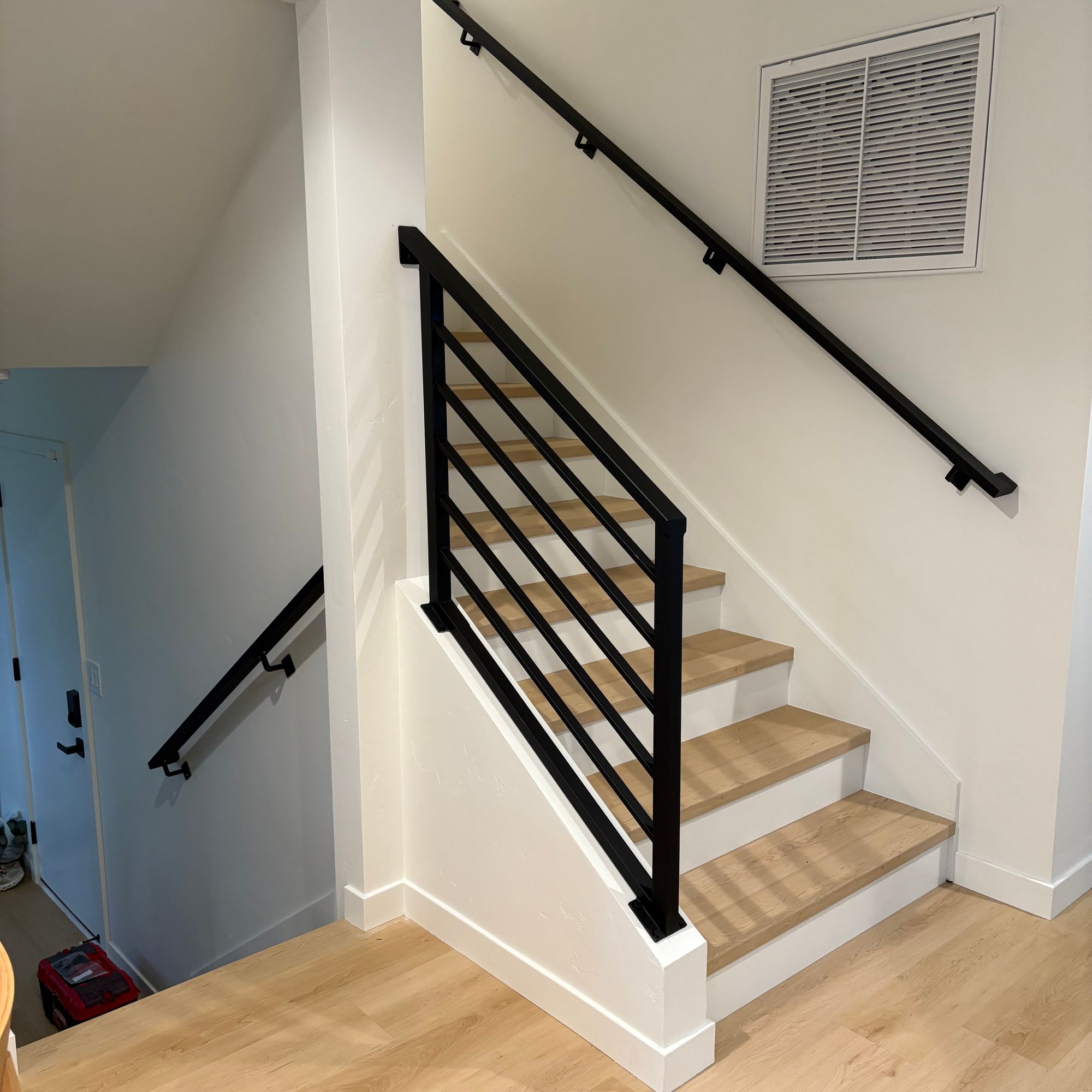 Modern staircase with black metal railings, wooden steps, and white walls in a contemporary home interior