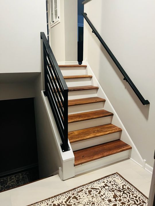 Modern staircase with wooden treads, white risers, black metal railing, and decorative area rug at the bottom