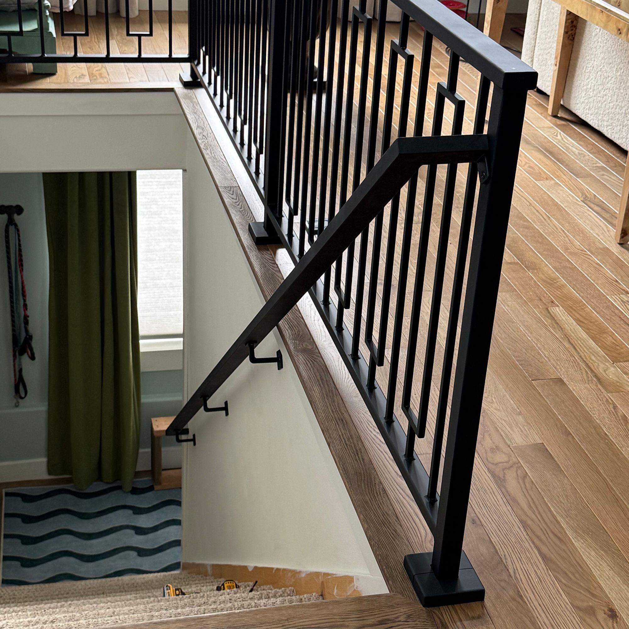 Interior staircase with black metal railing and balusters, wooden handrail, and hardwood flooring in a modern home