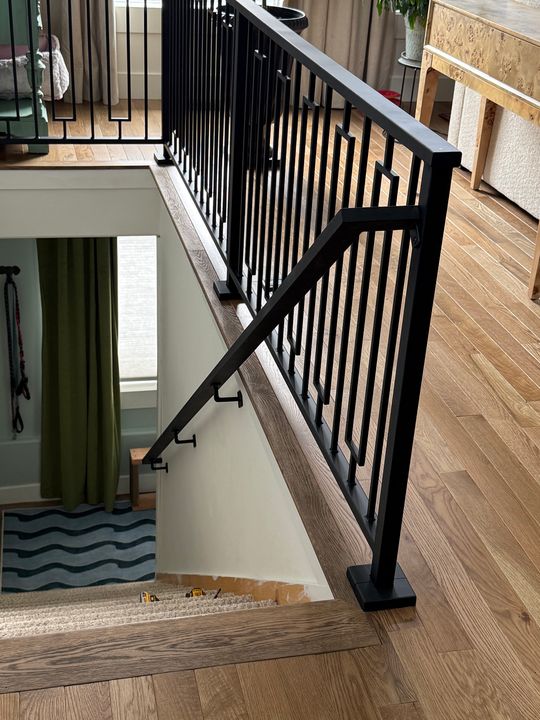 Interior staircase with black metal railing and balusters, wooden handrail, and hardwood flooring in a modern home