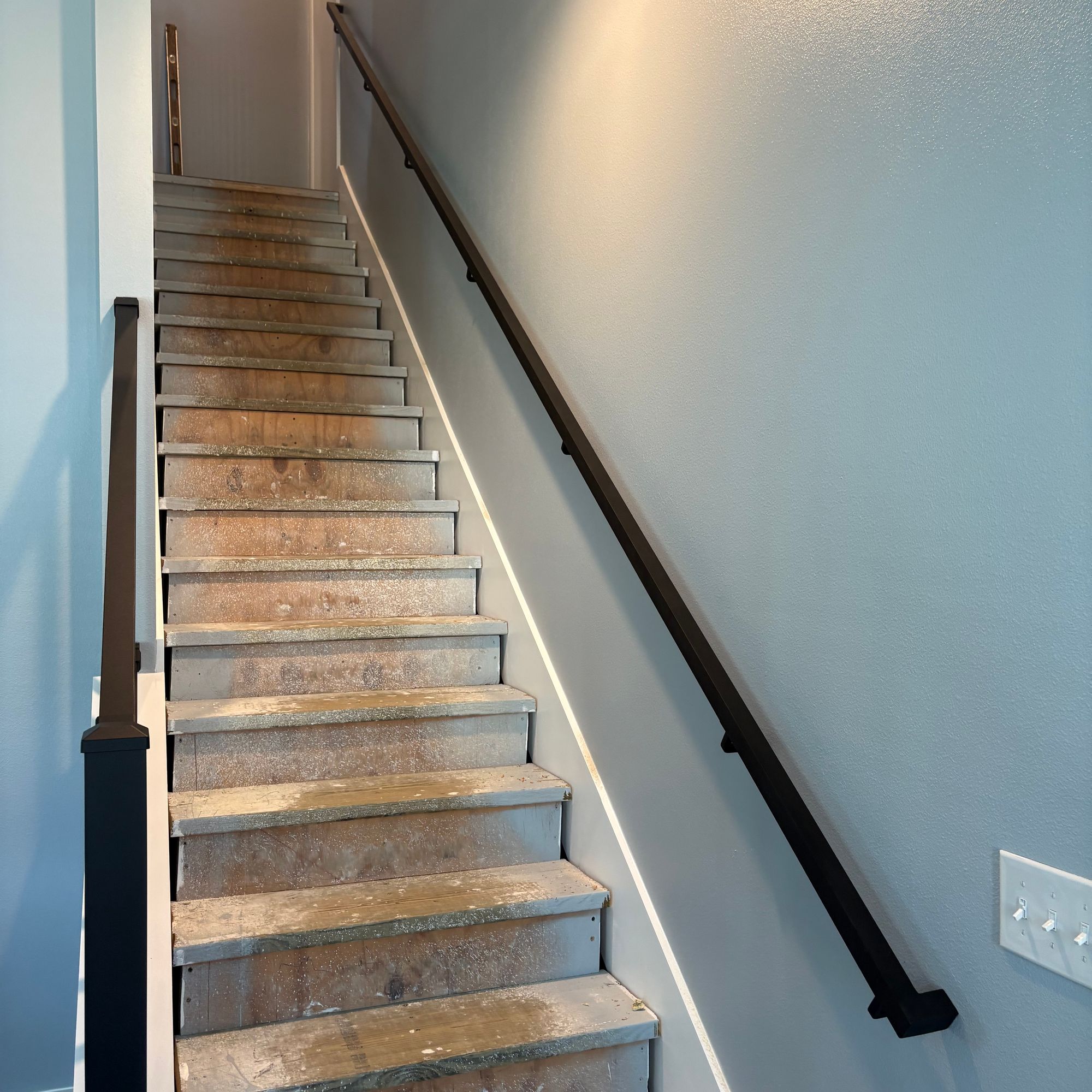 Interior staircase with wooden steps and black handrail leading upward in a home with light blue walls