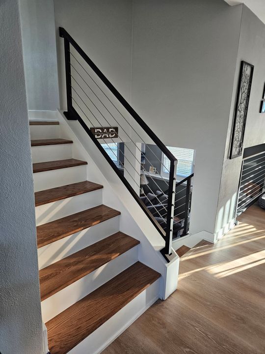 Modern staircase with dark wood treads, white risers, and black metal cable railing in a contemporary home interior