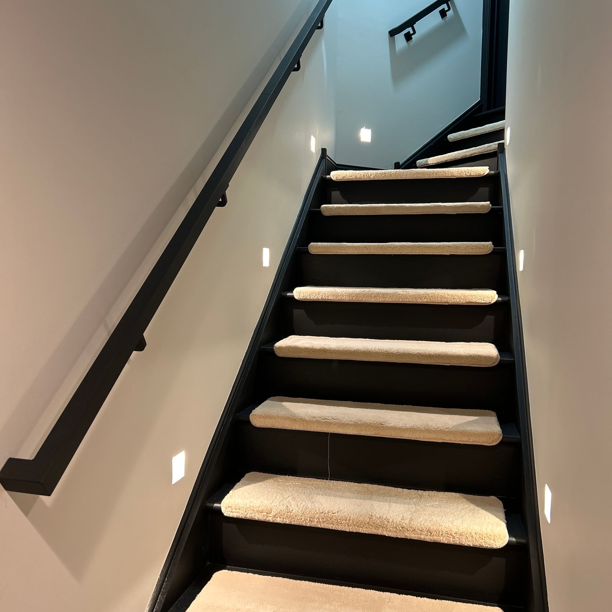 Modern staircase with black railings, light wood treads, and built-in LED lighting along white walls