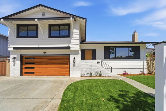 Modern two-story white house with wood garage door, large windows, and green lawn under blue sky