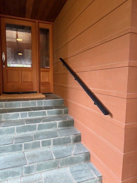 Stone steps leading to wooden front door with black handrail along orange exterior wall