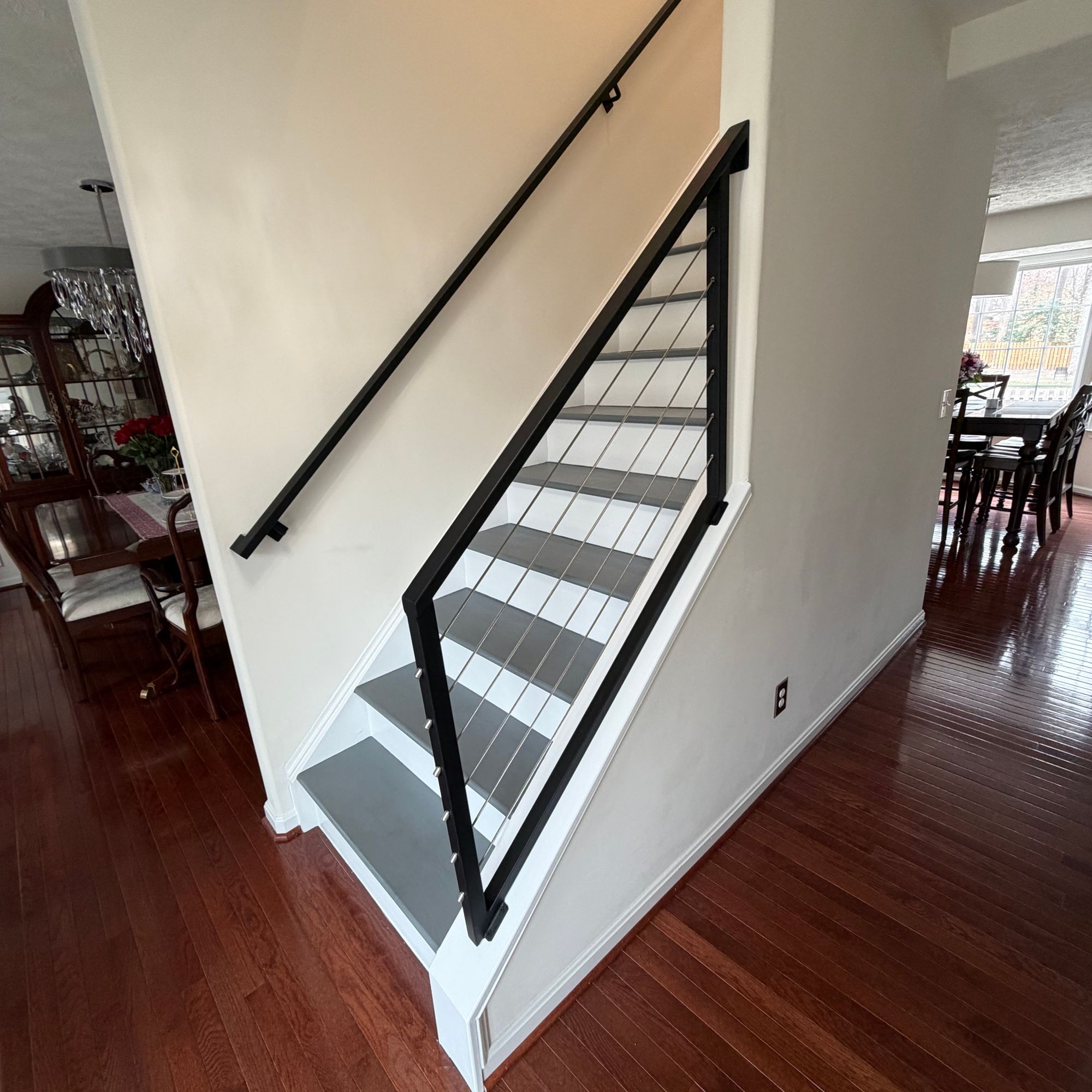 Modern staircase with black metal railings and white steps leading upstairs in an open-plan home with dark hardwood floors