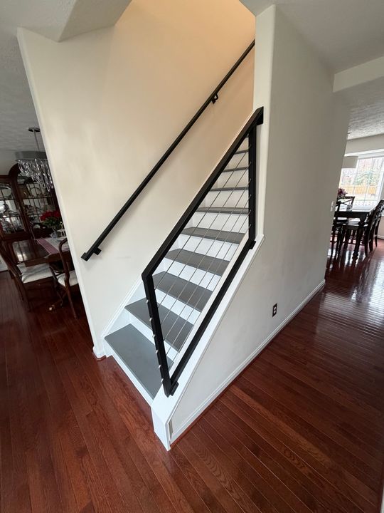 Modern staircase with black metal railings and white steps leading upstairs in an open-plan home with dark hardwood floors