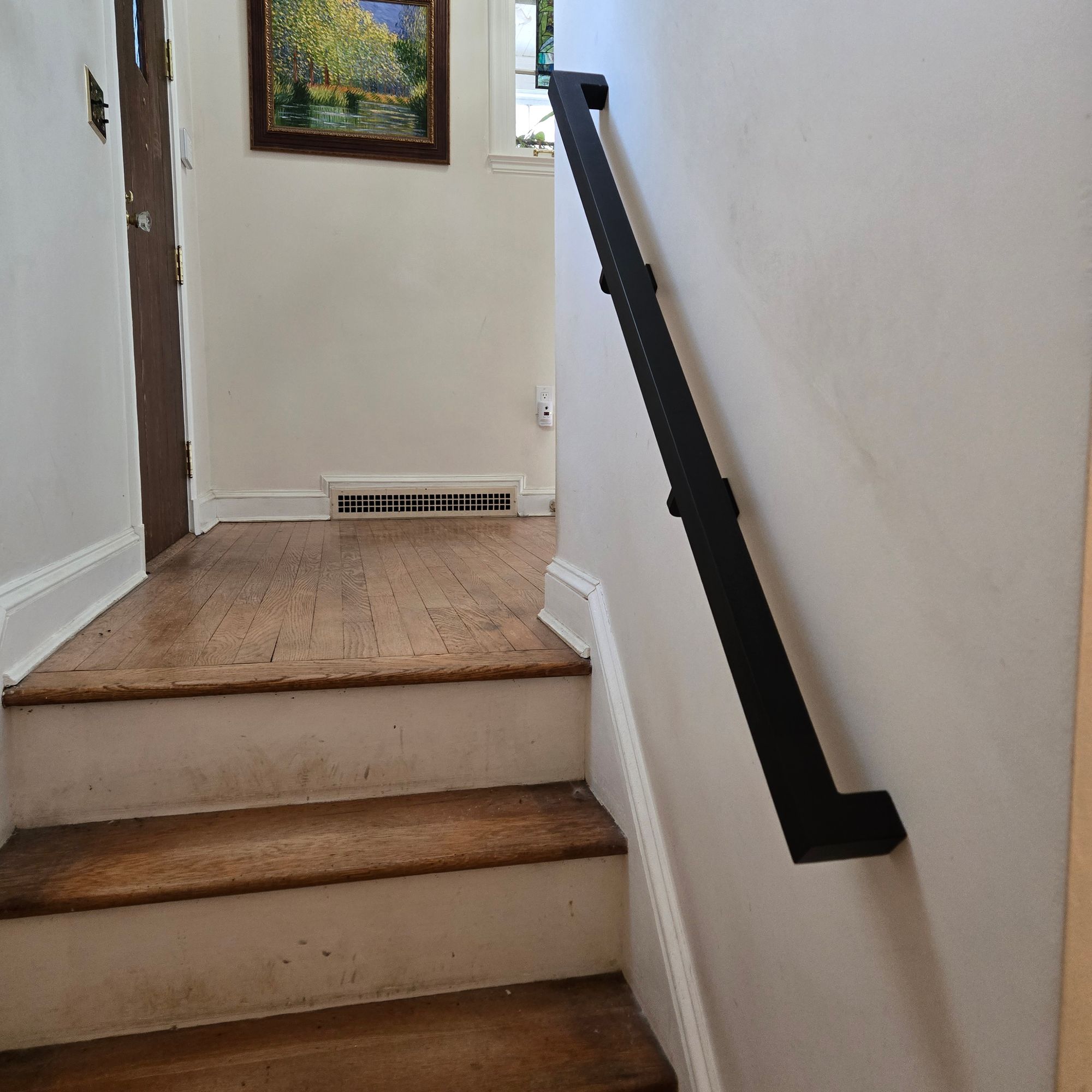 Interior staircase with wooden steps, white walls, black handrail, and framed artwork visible at the top landing