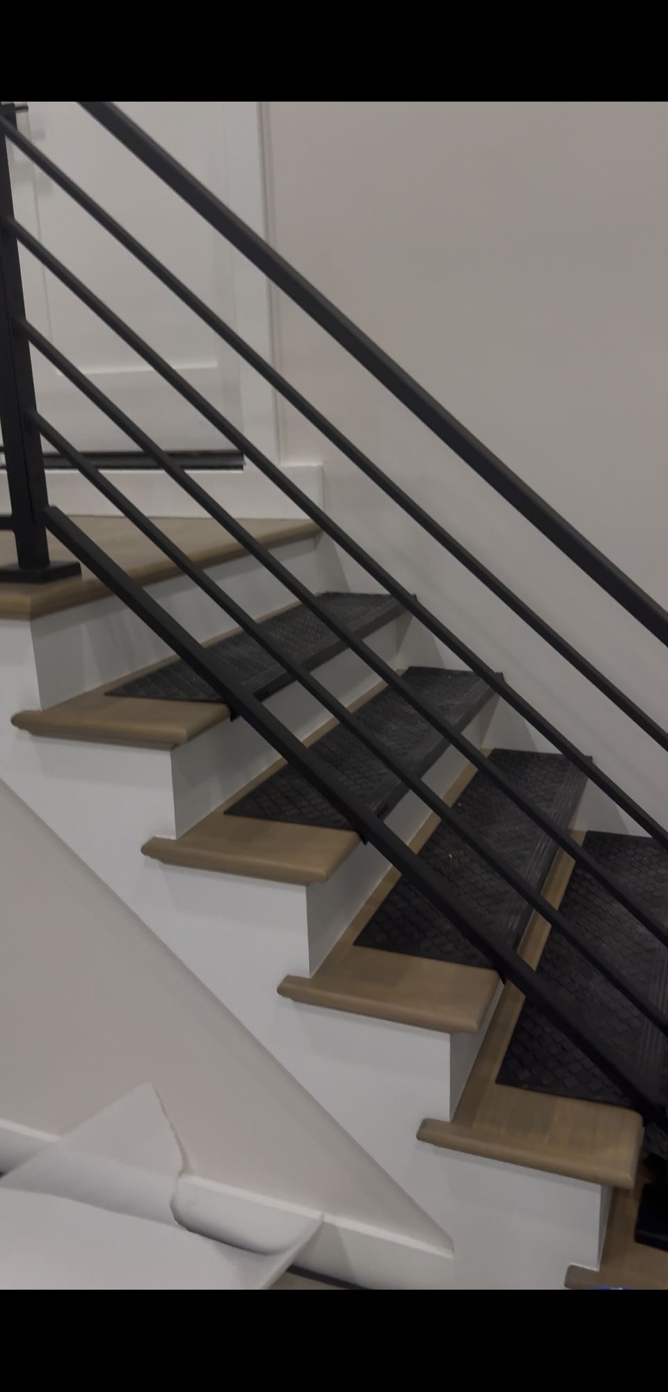 Modern staircase with wooden treads and black metal horizontal railings in a white interior space