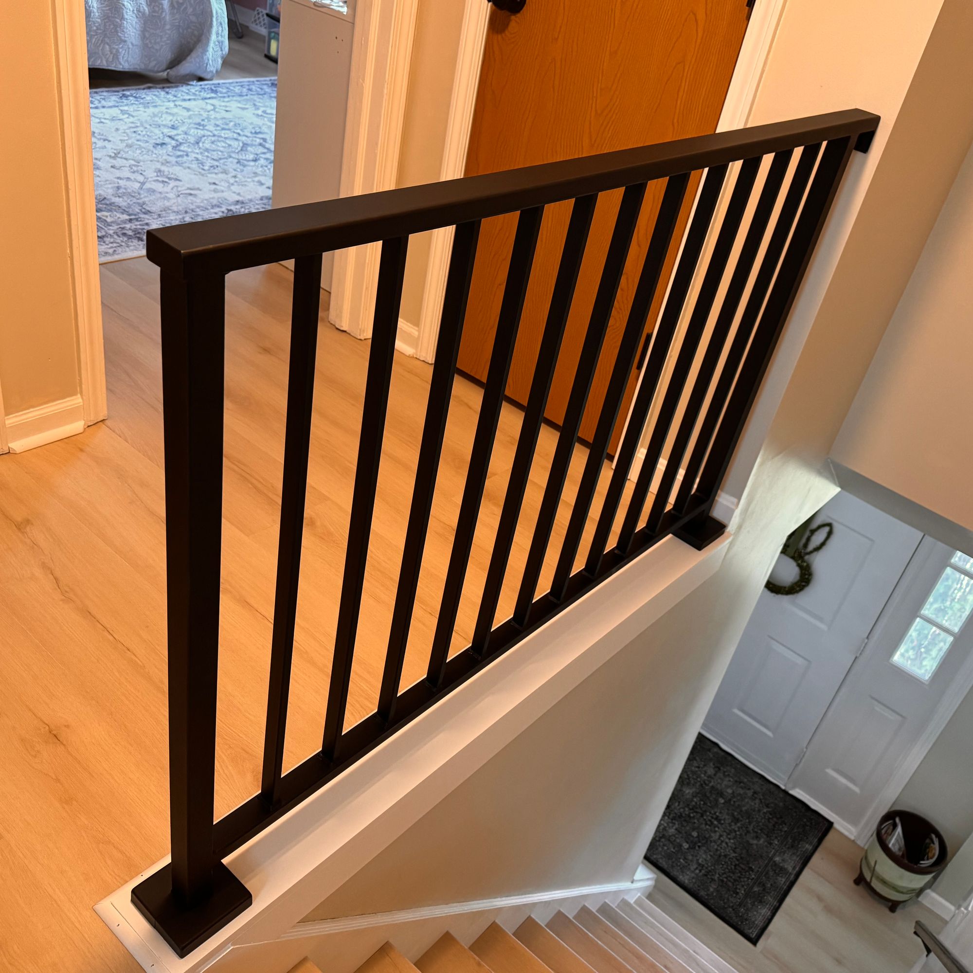 Interior staircase with dark wooden railing and vertical spindles overlooking an entryway with white door and dark floor mat